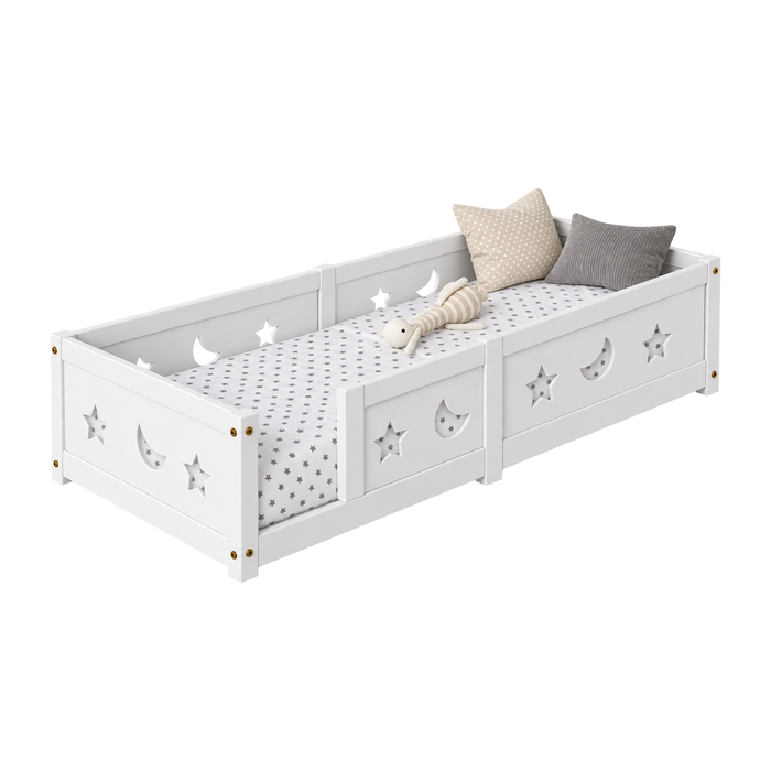 Lit Montessori au sol Belmia modèle A1 sans barrière, panneaux latéraux bas ajourés de motifs étoiles et lunes, vue de trois quarts sur fond blanc